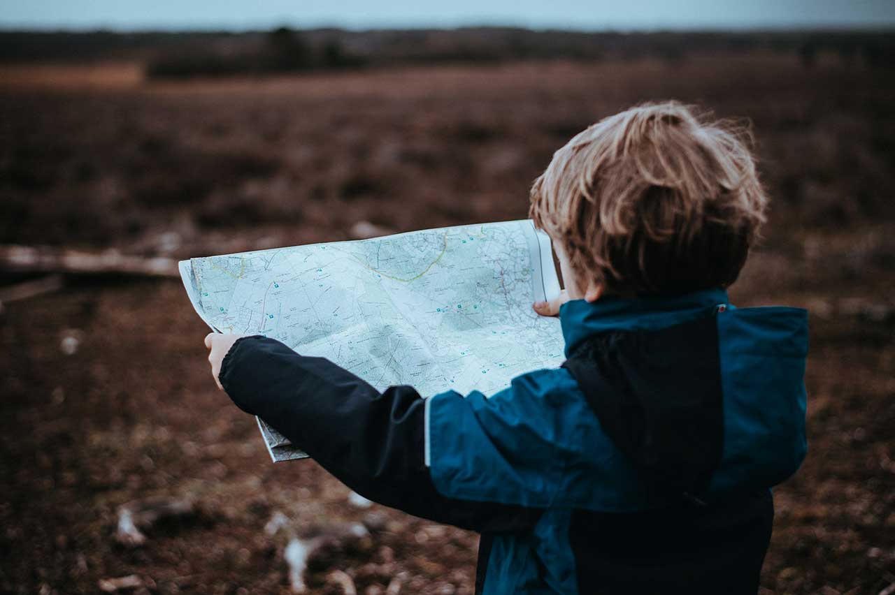 A small boy holds up a map with the countryside visible behind