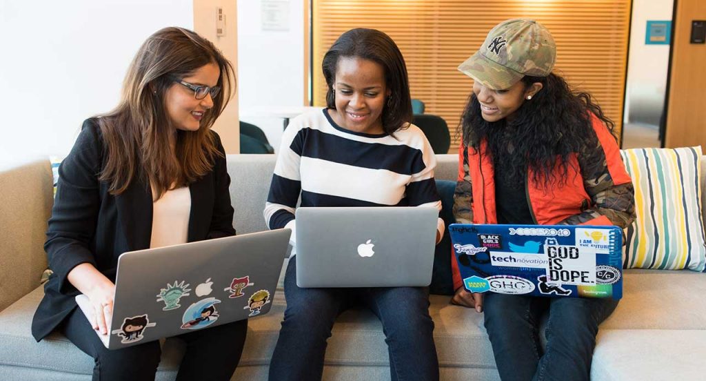 Three women using laptops and sitting on a sofa