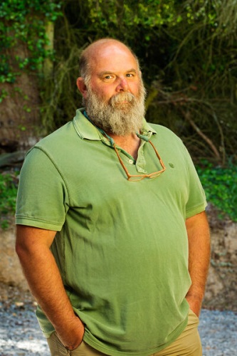 A bearded man in green shirt by a river bank