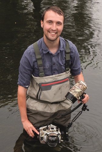 A man in waders standing in a river with an underwater camera