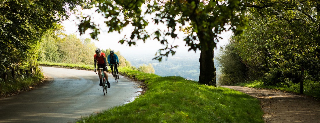 Two cyclists in lycra round a dramatic hilltop corner on a country road
