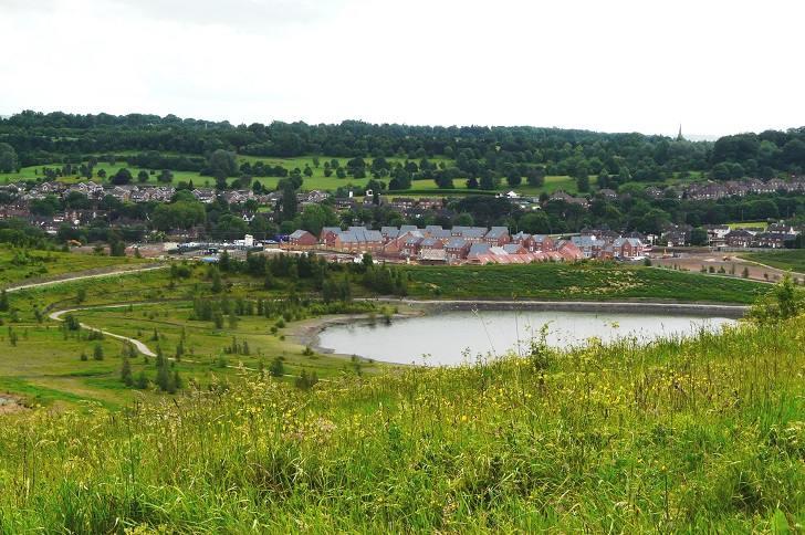 A large pool surrounded by green space with a housing on the far side