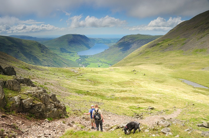 Two walkers and a dog on a footpath in a wide upland valley