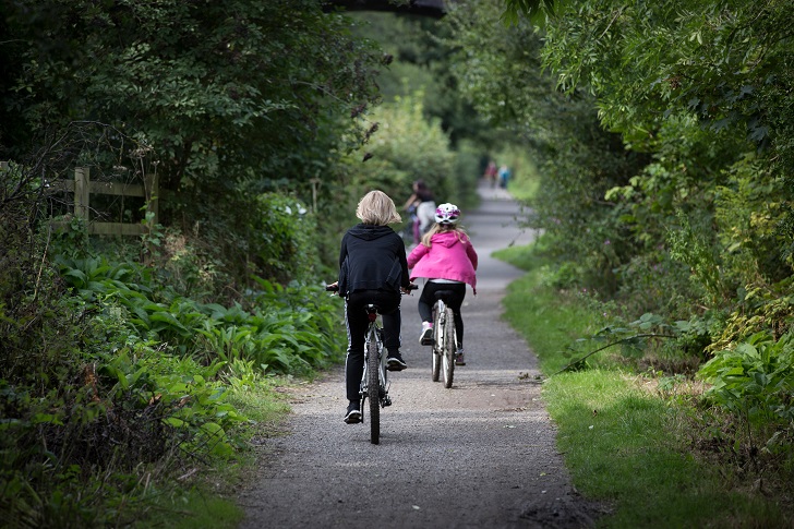 Two young people cycling along a path surrounded by trees