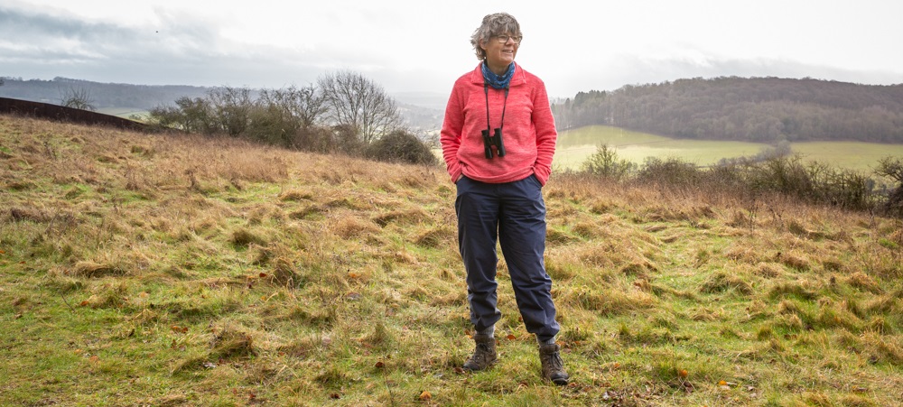 A woman on a misty green moor with pink jumper and binoculars