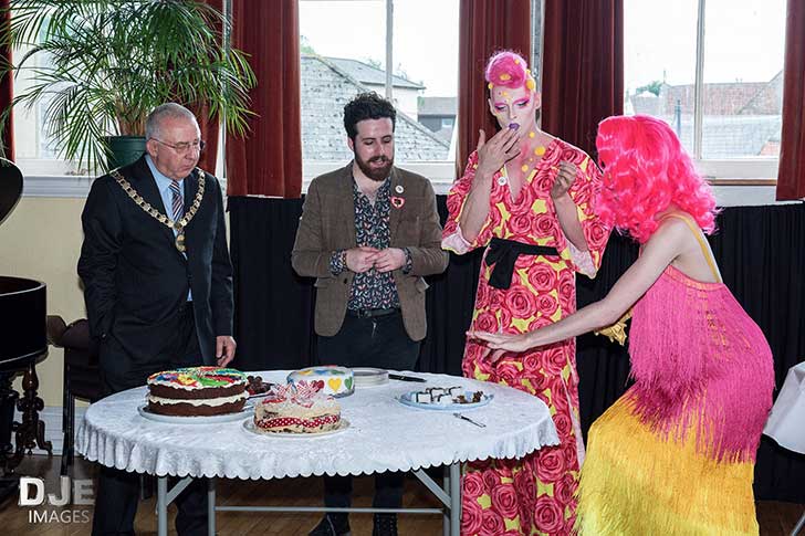 Two drag queens and two men stand at a table tasting cake