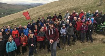 Large group of walkers gather on hillside with Ramblers flag