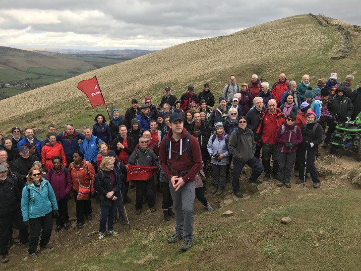 Large group of walkers gather on hillside with Ramblers flag