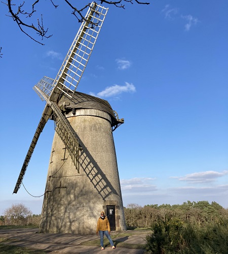 A stone clad windmill on top of a hill under a blue sky