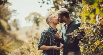 Two men kiss as they pick blackberries from a hedgerow