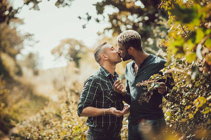 Two men kiss as they pick blackberries from a hedgerow