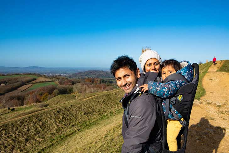 A young man and woman on a hilly ledge with a small child in a carrier