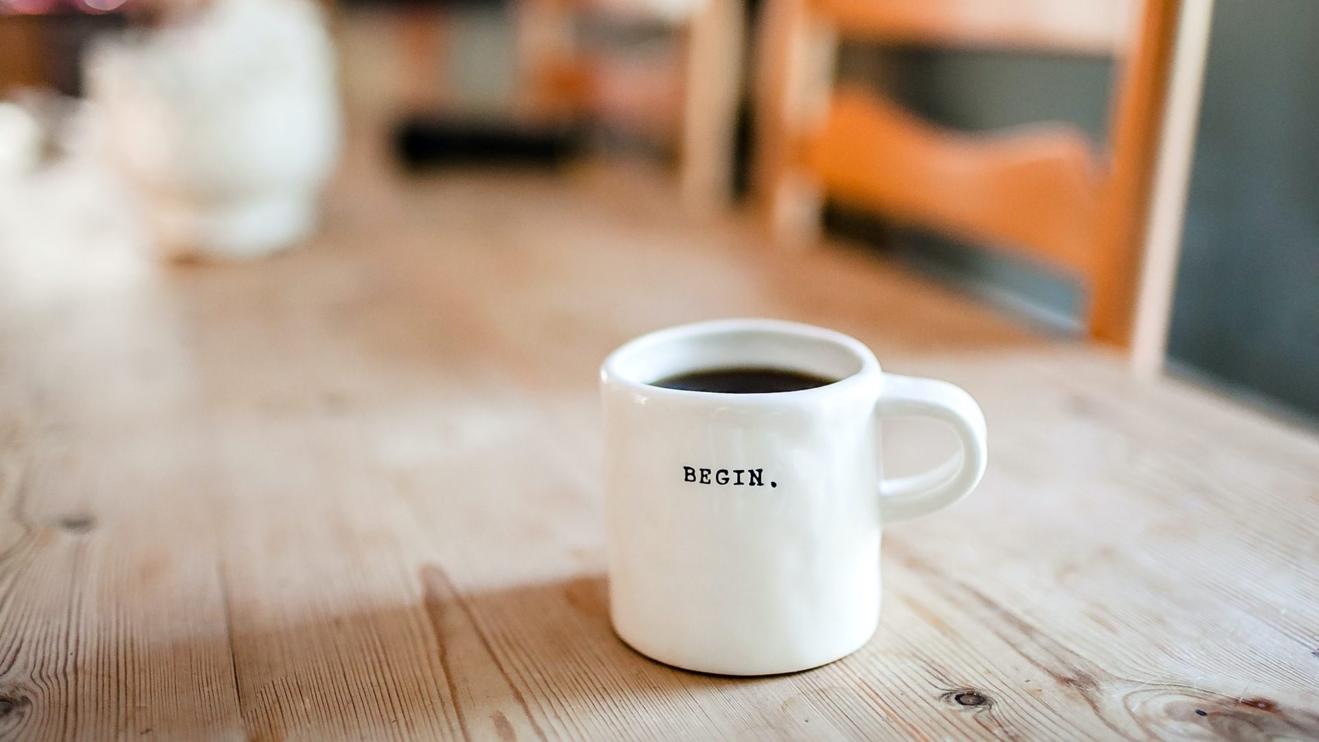A white mug on a pine table with the word 'begin' on it