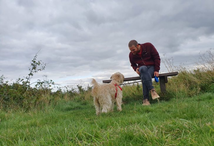 Man sat on bench in countryside with dog looking up at him