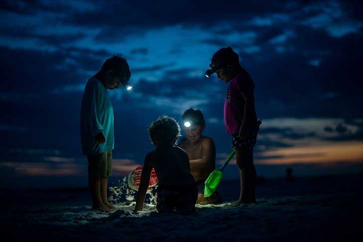 Four children on a beach at sunset wearing headtorches