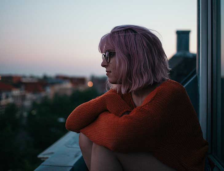 A girl sits cross-legged on a roof as the sun sets