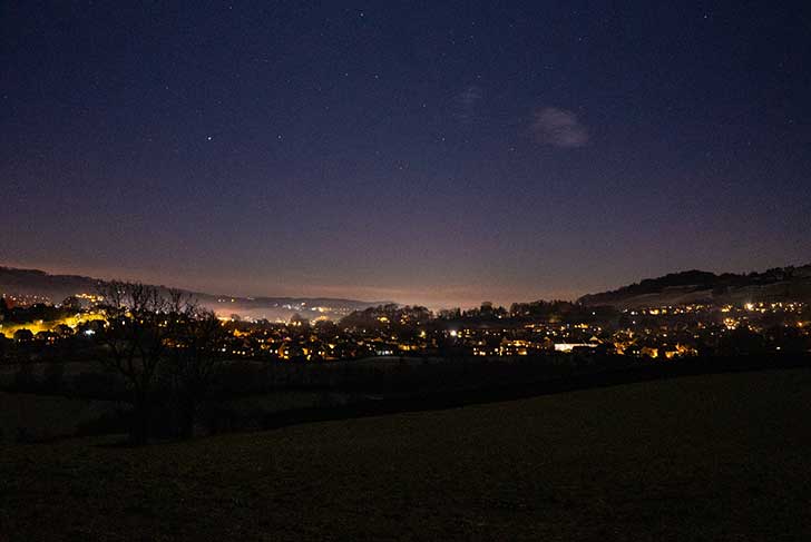 A dark valley with a town visible, with glowing light pollution