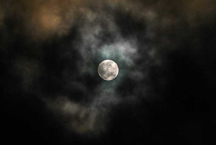 A bright glowing full moon with clouds passing over