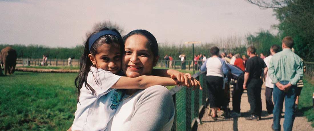 A mother holds her child in her arms with sunny green spaces behind