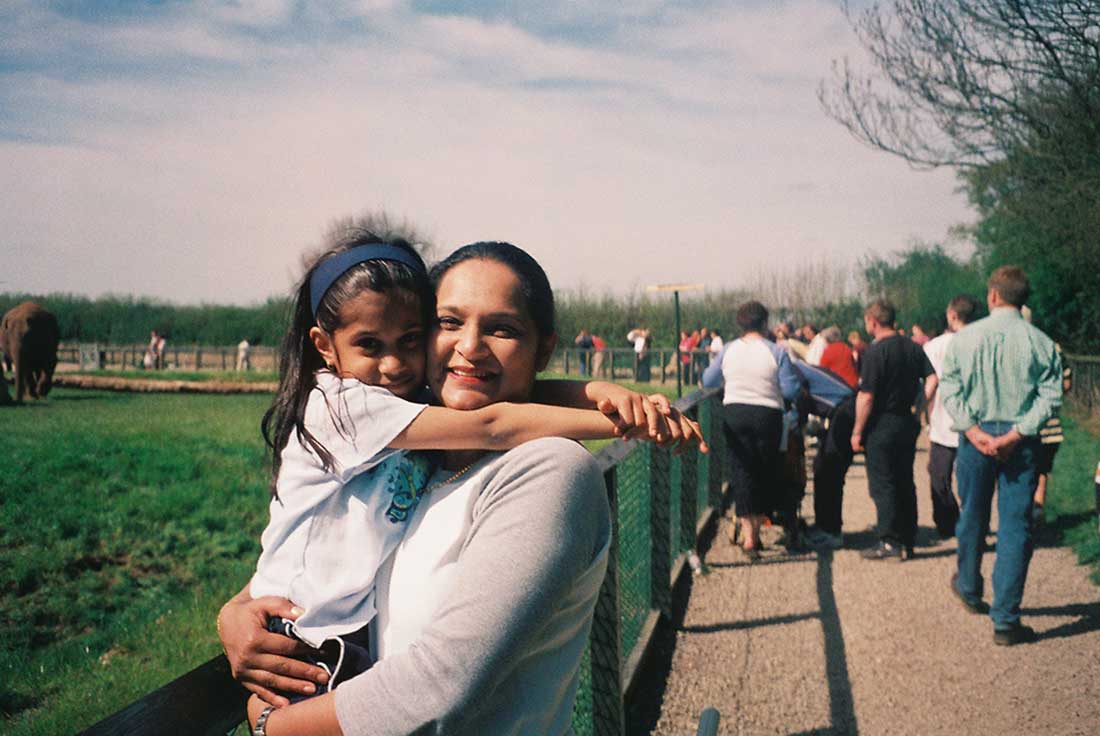 A mother holds her child in her arms with sunny green spaces behind