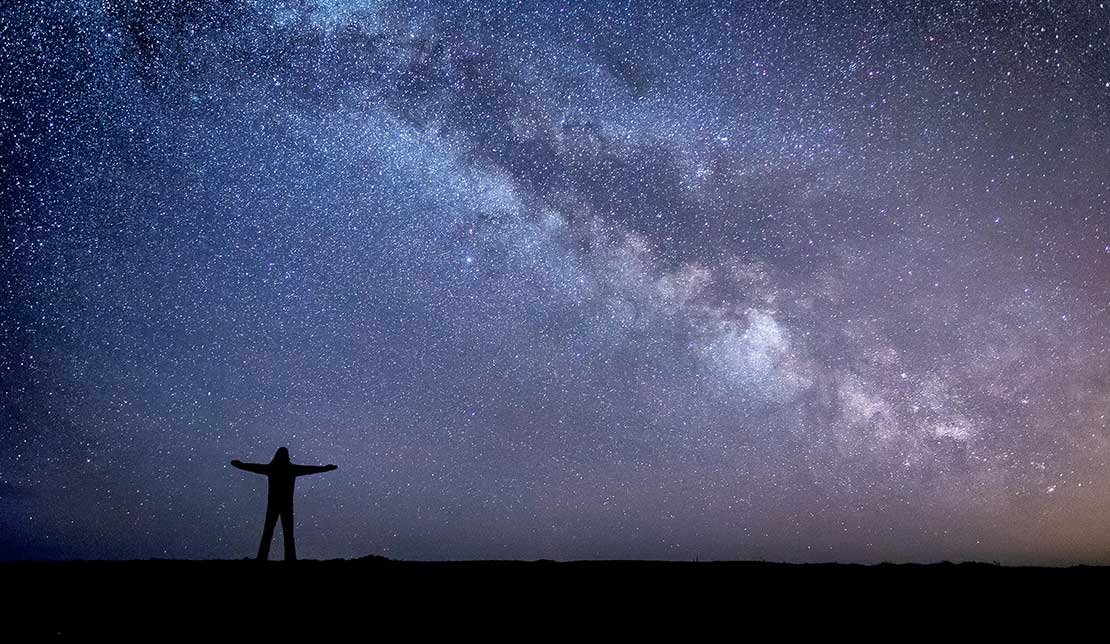 A figure silhouetted against a starry sky showing the Milky Way