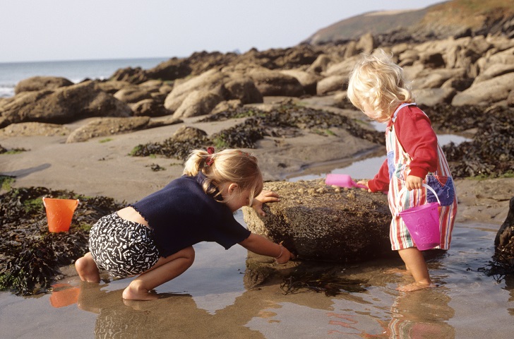 two young girls with buckets in a beach rock pool