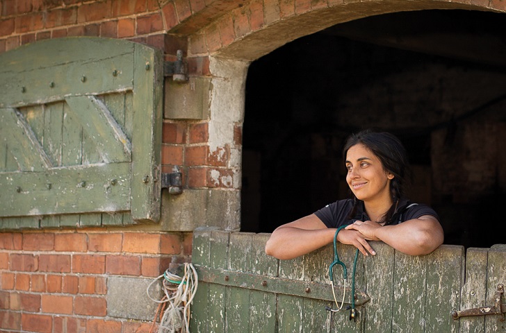 A woman in a stable looking out leaning over the door