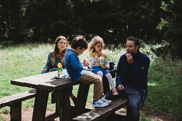 family shares a picnic on a bench outdoors