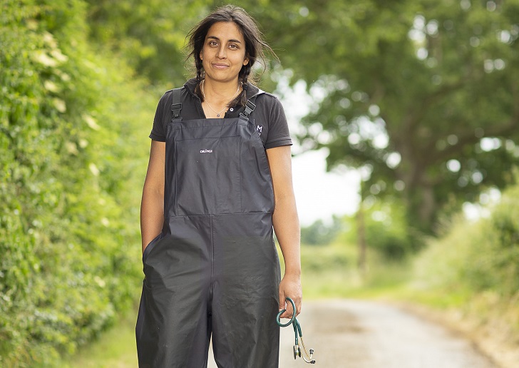 A woman in vets overalls standing in a hedge-lined lane