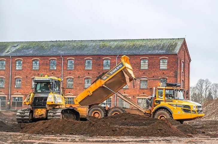 A building site with old red brick buildings with yellow diggers in front