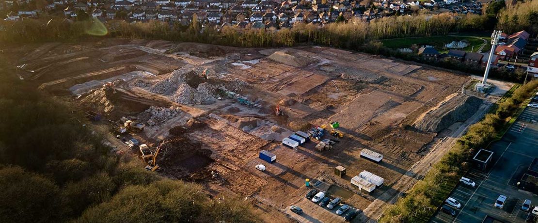 Aerial view of brown building site land with fields and houses around