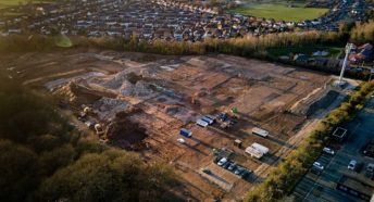 Aerial view of brown building site land with fields and houses around