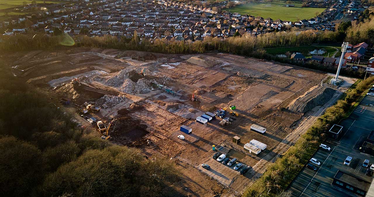 Aerial view of brown building site land with fields and houses around