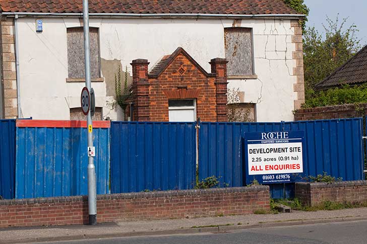 A boarded up building with hoardings and a For Sale sign