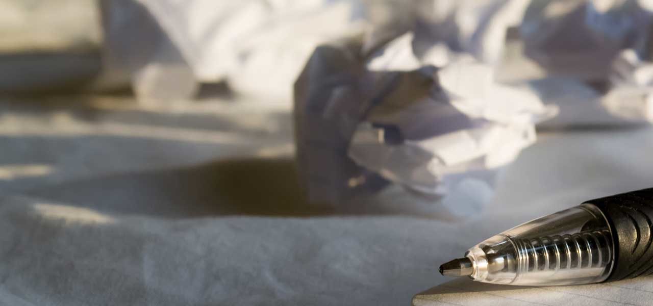 Crumpled up pieces of white paper beside a notebook and pen