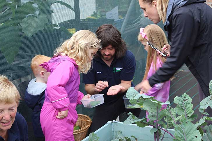 Children sit with a gardener and explore seeds in a garden