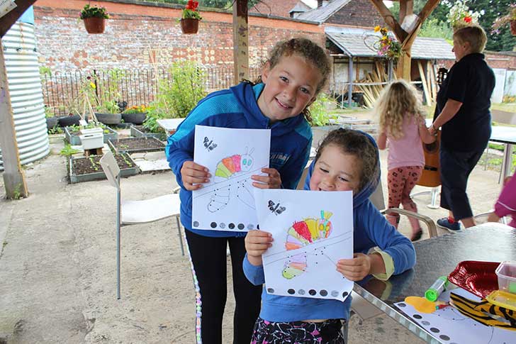 Children in a garden showing pictures they've coloured in