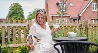 A woman sits in a garden with houses visible behind and pets a dog