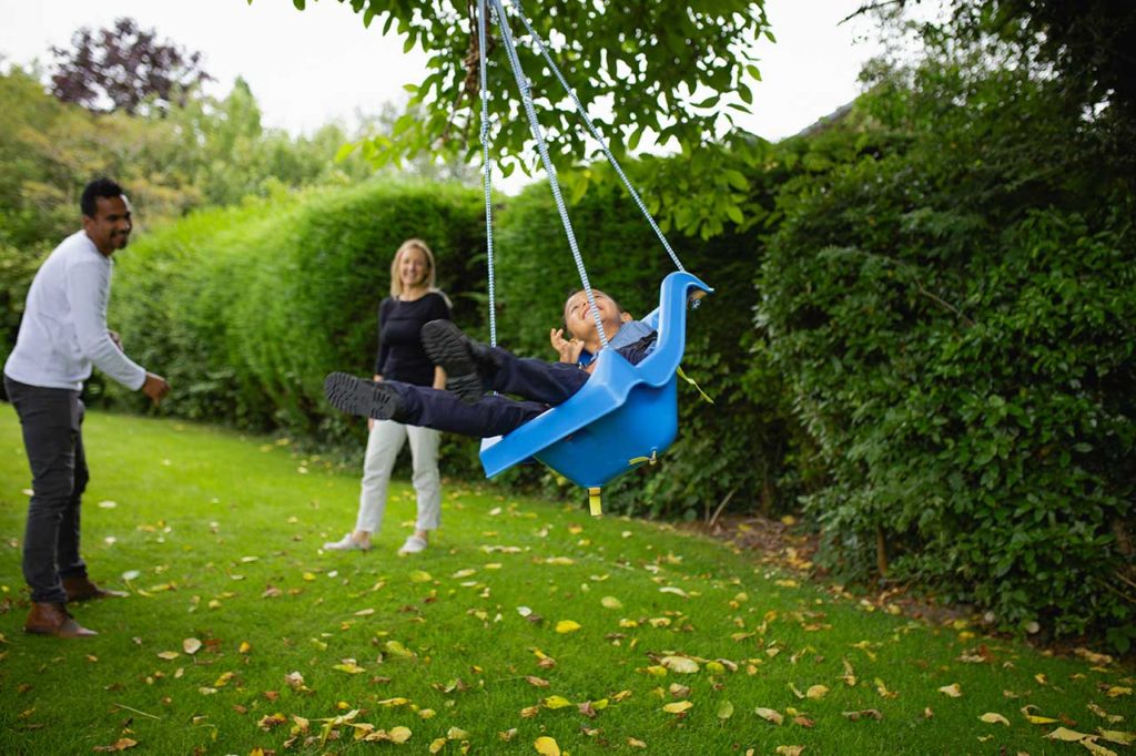 A man and woman push a small boy on a bright swing