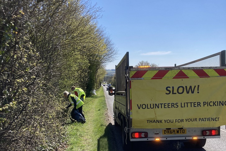 People picking litter on a roadside with a hedgerow and van