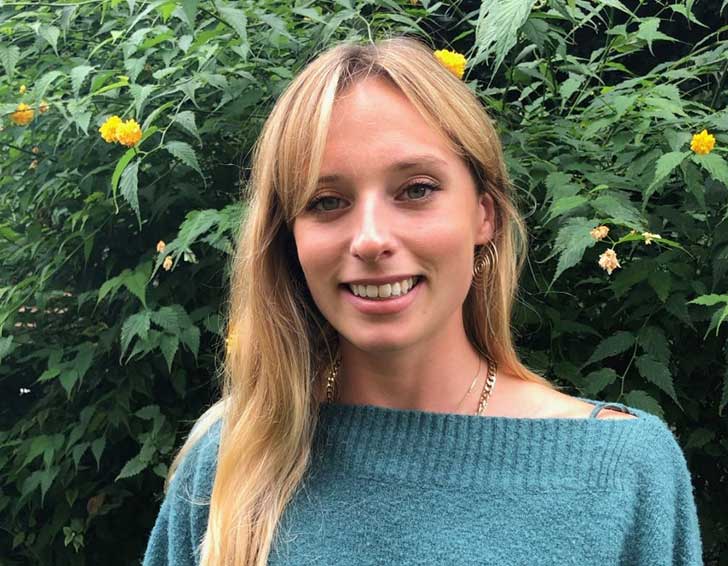 A young blonde woman in a green jumper smiles at the camera