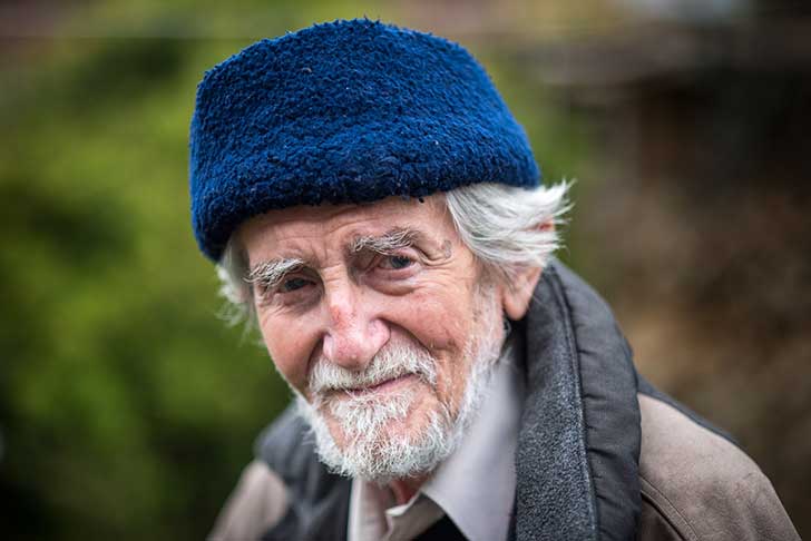 An older man outdoors, with white hair and a bright warm hat