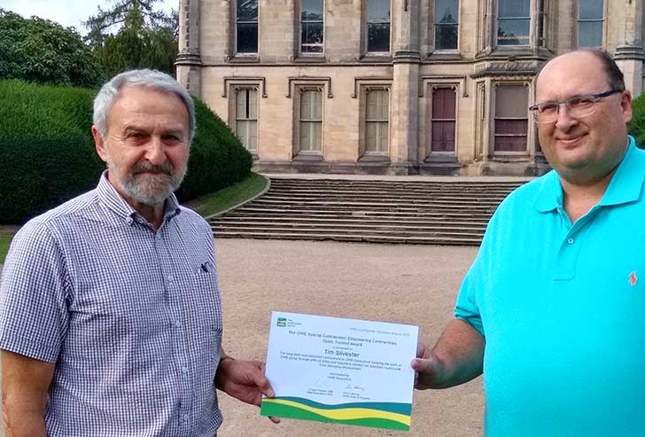 Two men look at the camera and hold a certificate between them