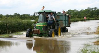 A tractor with some passengers drives on a flooded rural lane