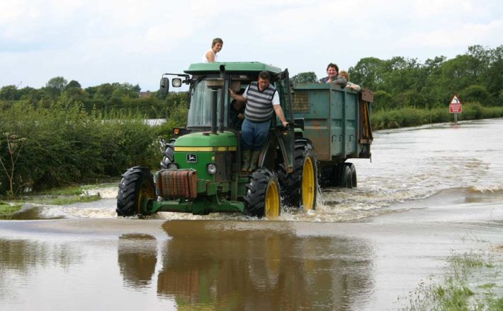 A tractor with some passengers drives on a flooded rural lane