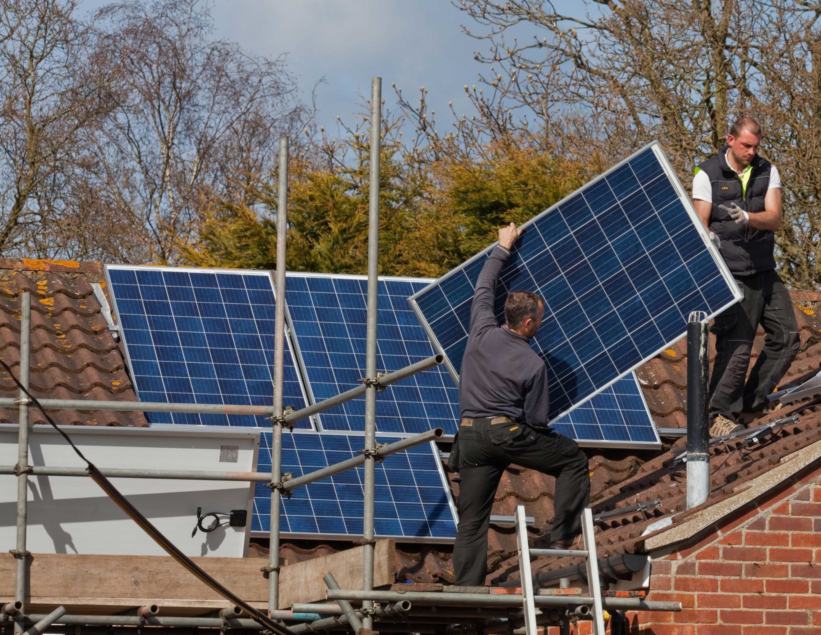 Two men on a tiled house roof lifting solar panels to attach