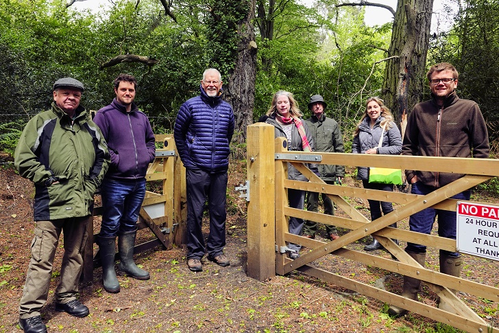 A group of people standing by a farm gate in woodland