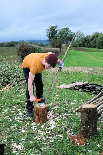 A boy sharpening the end of a wooden stake in the countryside