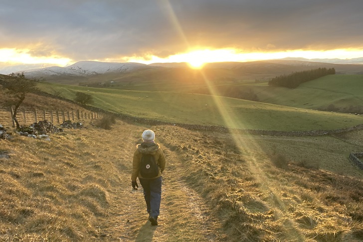 A woman walking into the sunset on a green hillside