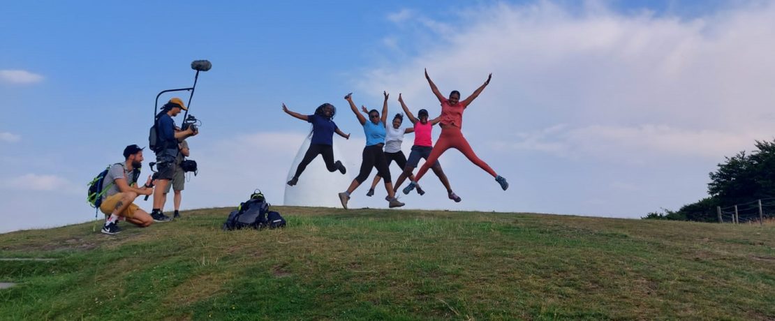 a camera screw filming a group of women jumping in the air on the top of a green hill